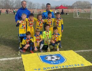 ФК Димитровград 1947 с два отбора на турнира „Изкупи ме“ в Хисаря ФК Димитровград 1947 взе участие на турнира „Изкупи ме“ в Хисаря с два отбора от набор 2016 — жълт и син. Малките футболисти показаха голям хъс и неизменно усмивки, които понякога струват повече от всяка купа. След силни срещи, много голове и отличен отборен дух, жълтите заслужено спечелиха турнира. Браво, момчета! Синият отбор се бореше до последно и завърши на 5-то място. Всеки мач беше урок, а всяка минута — стъпка напред. Най-ценното от състезанието бяха усмивките, новите приятелства и истинските футболни спомени — там се гради бъдещето на клуба. Гордеем се с вас, шампиони! Продължавайте да играете със сърце!