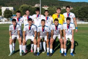 Олимпик (Варна) победи Устрем (Дончево) с 4:3 в първия кръг на Североизточната Трета лига Олимпик (Варна) започна сезона 2026/27 с драматична победа, надделявайки с 4:3 като гост на Устрем (Дончево) в първия кръг на Североизточната Трета лига. Варненци откриха резултата рано чрез Юксел Алиев (7'), но домакините бързо възстановиха равенството след дълга топка и гол на Дейвид Венциславов (12'). В 31-ата минута при нова дълга топка Александър Грозев надскочи вратаря и Иван Бориславов се разписа на празна врата с глава. В следващата атака Устрем отново изравни след подаване между централните бранители и гол на Виктор Христов. Второто полувреме предложи няколко отлични положения за гостите — Бориславов стреля с глава от пет метра и нацели гредата, а малко по-късно Владислав Георгиев намери вратаря Никола Терзиев. В 75-ата минута домакините направиха пълен обрат след атака отдясно и разбъркване в наказателното поле, при което опитният Иван Цачев бе най-съобразителен. Устрем имаше още един шанс да направи резултата 4:2, но пропусна, а в самия край младите футболисти на Олимпик постигнаха обрат. В 91-ата минута Иван Марков получи топката на точката за дузпата и с хубав удар изравни. След изпълнението на центъра варненци откраднаха топката и в контраатака при удар на Юксел Алиев последва двоен рикошет, след който Александър Гроздев прати топката в мрежата. В този момент реферът свири край на срещата. Олимпик зарадва феновете си въпреки отсъствието на контузения Никола Стоянов. В междинния втори кръг тимът от Варна приема новака Септември (Драгоево). Двубоят е в сряда, 26-ти август, от 18:00 часа на стадиона на Национална спортна база „Спортпалас“ в курорта Златни пясъци.